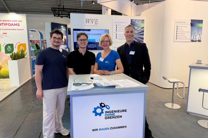 Vier Menschen sind auf einer Messe hinter einem Stand und lächeln in die Kamera