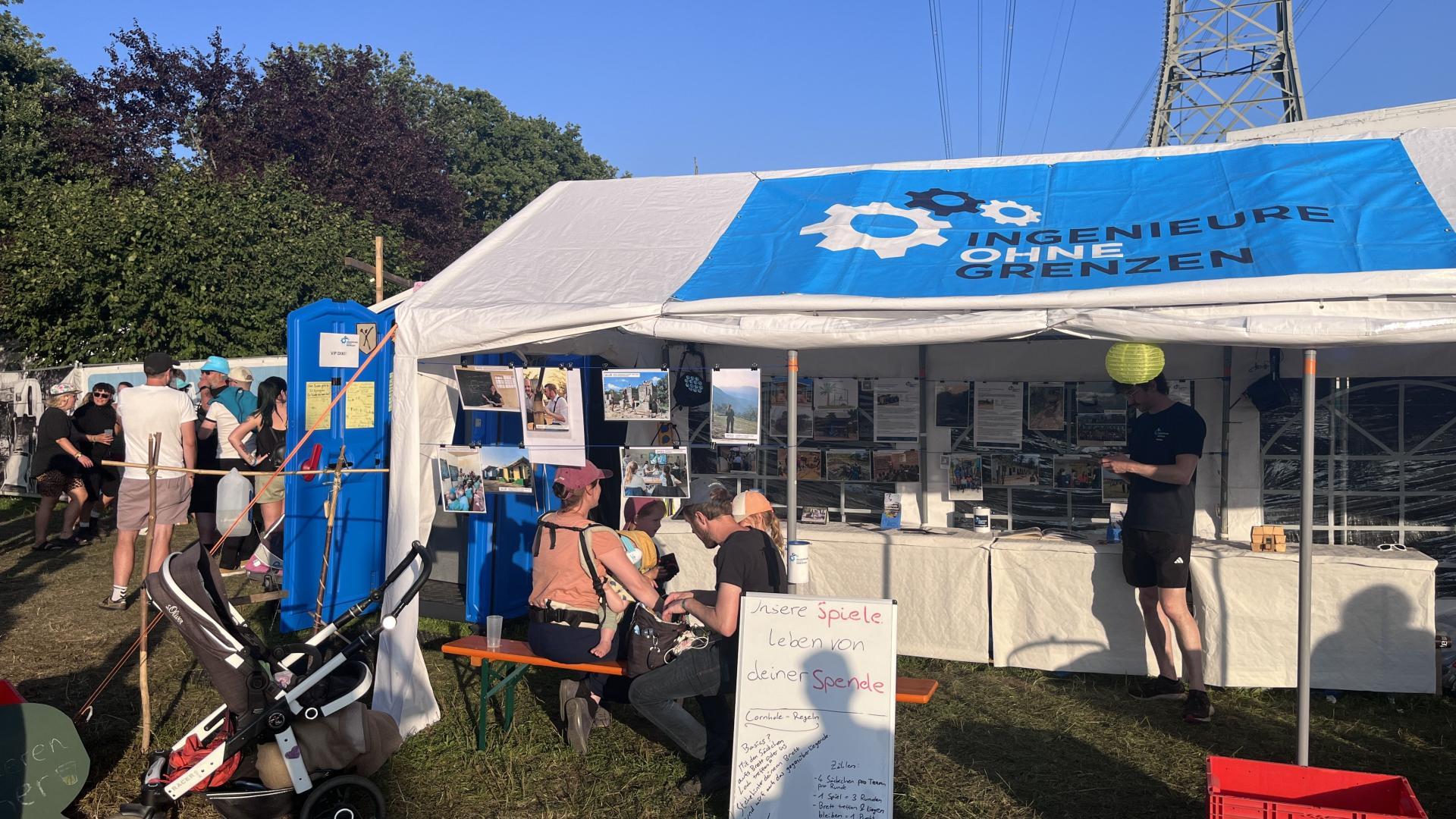 Informationsstand von IOG auf einem Festivalgelände. Menschen stehen interessiert vor dem Zelt.
