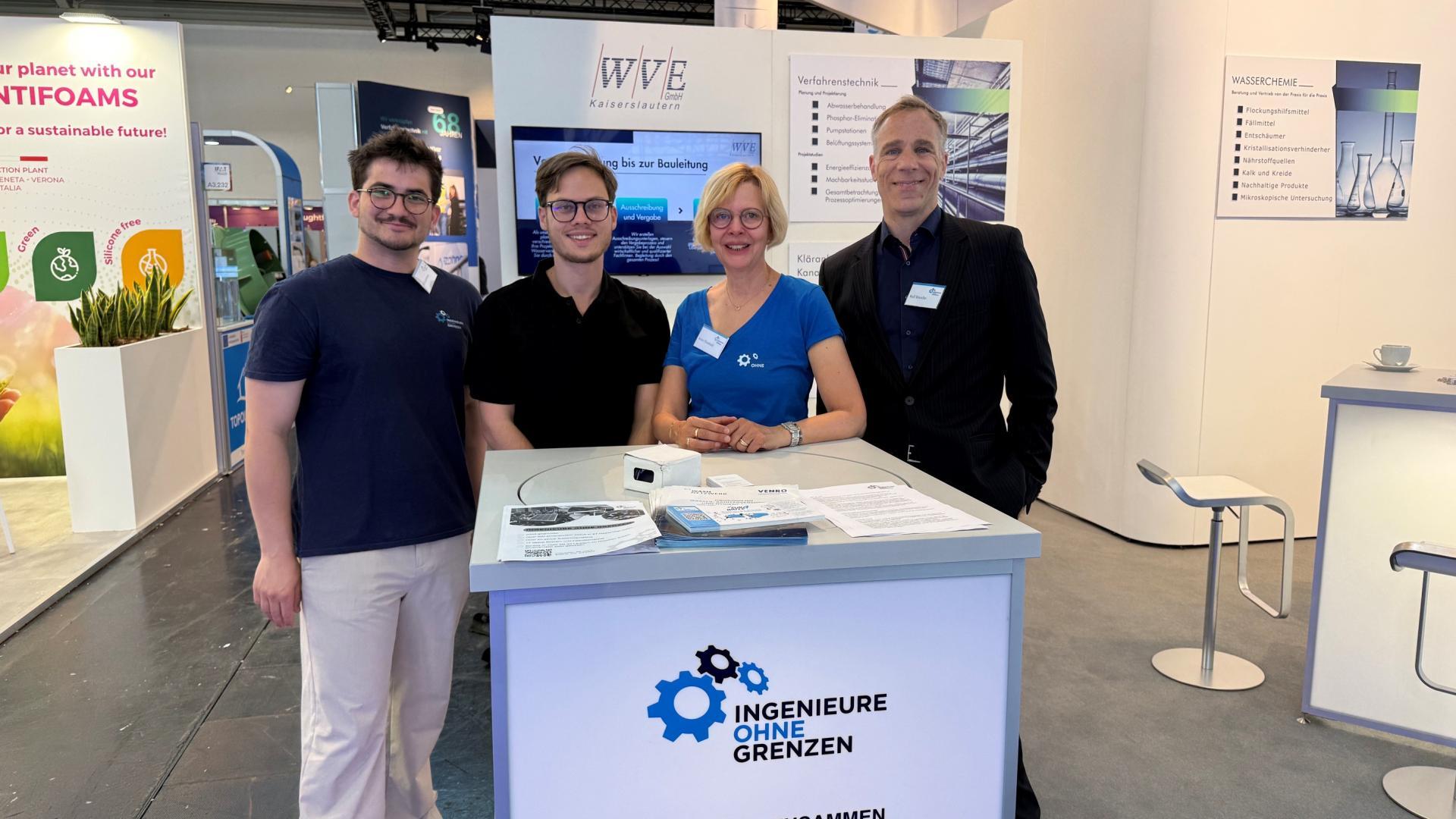 Vier Menschen sind auf einer Messe hinter einem Stand und lächeln in die Kamera